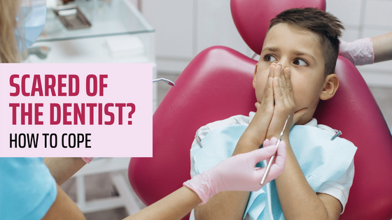 Boy with hands over his mouth sitting in a dental chair while a dentist holds tools nearby