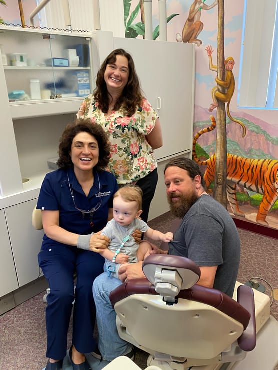 Dr Zahedi smiling with a yound toddler during a pediatric dental appointment alongside the toddlers parents